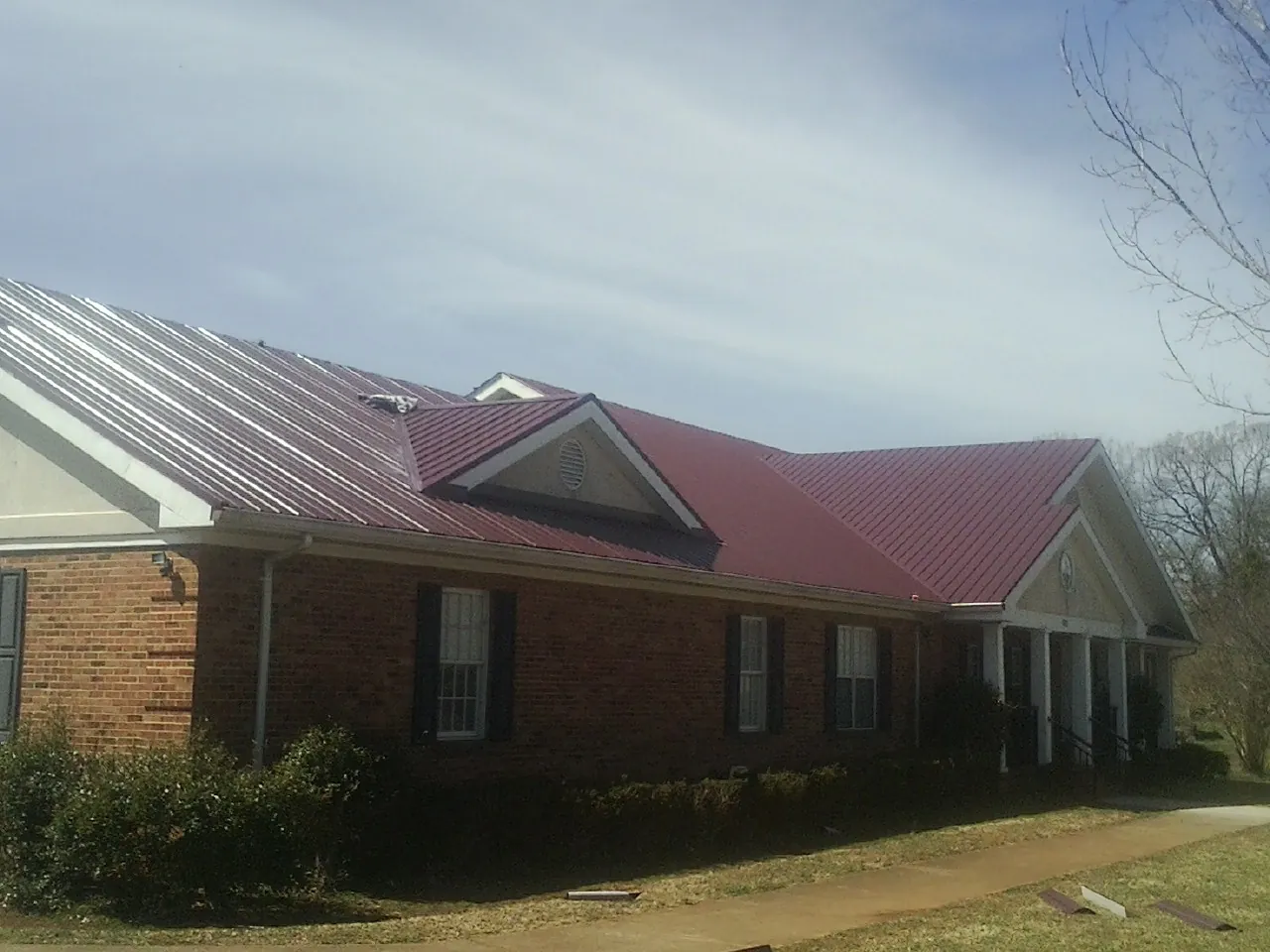 Red metal roof with gabled entries on a long brick building, from a Hail Damage Roof Repair job in Metairie