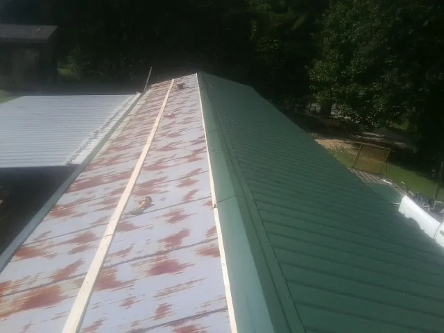 Old rusted panels beside newly installed green metal roofing — Wind Damage Roof Repair by Roofing Brothers in Metairie