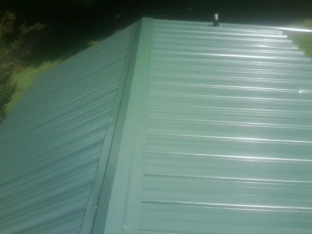 New green metal panels meeting at the ridge of a roof — Flat Roof Repair work by our crew in Metairie