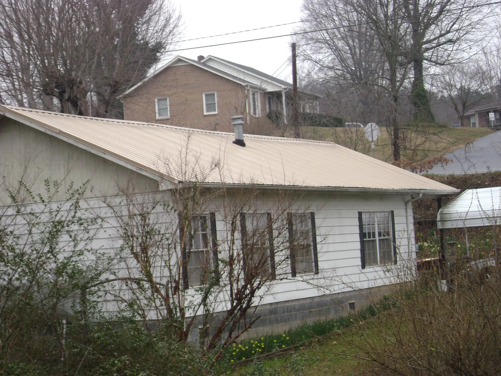 Tan metal roof on a white sided house set into a hillside — Commercial Roofing by Roofing Brothers in Metairie