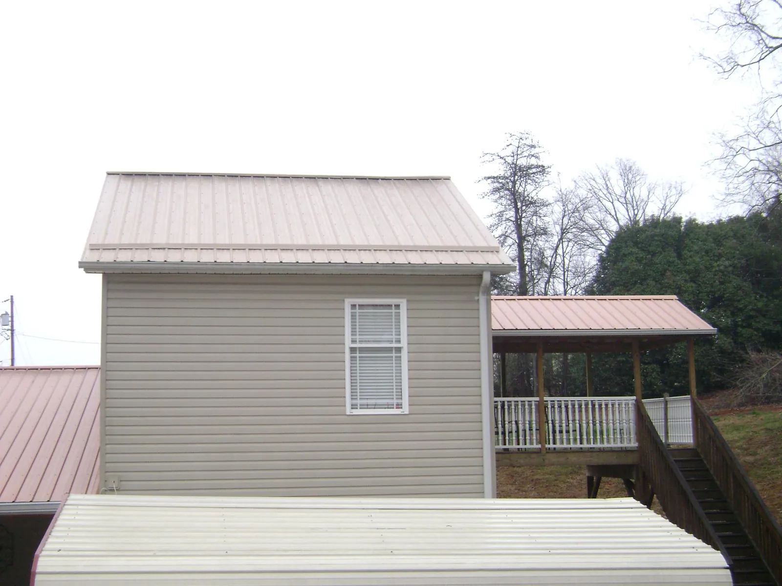 Tan metal roofs on a two story addition and attached porch, from a Roof Replacement job in Metairie